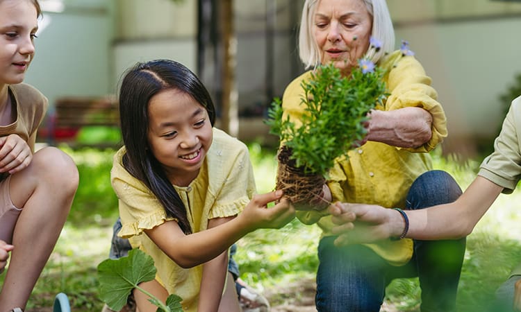 A young girl smiles while a teacher shows her a plant